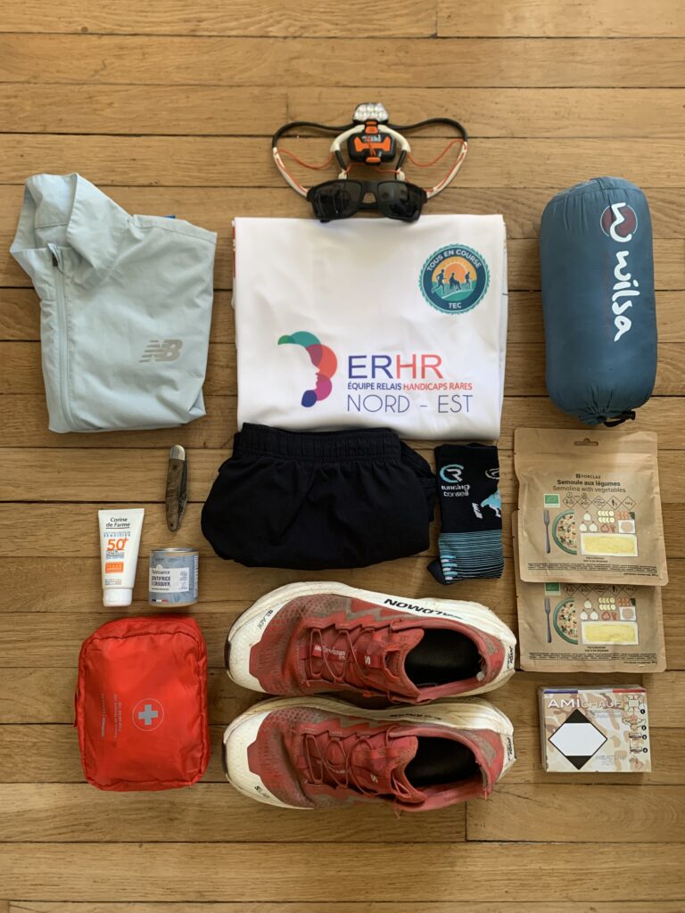 Aperçu des premières affaires qu'Adrien emportera pour la course : vêtements, paire de baskets, sac de couchage, repas lyophilisés, canif, trousse de secours, lunettes de soleil.